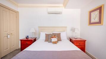 Une chambre d’hôtel avec un grand lit, deux tables de chevet, une commode rouge, un climatiseur fixé au mur et un tableau encadré accroché au mur.