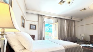 A hotel room with a large bed, a desk, a chair, and a view of the outdoors. - Cobb & Co Court Boutique Hotel (Mudgee)