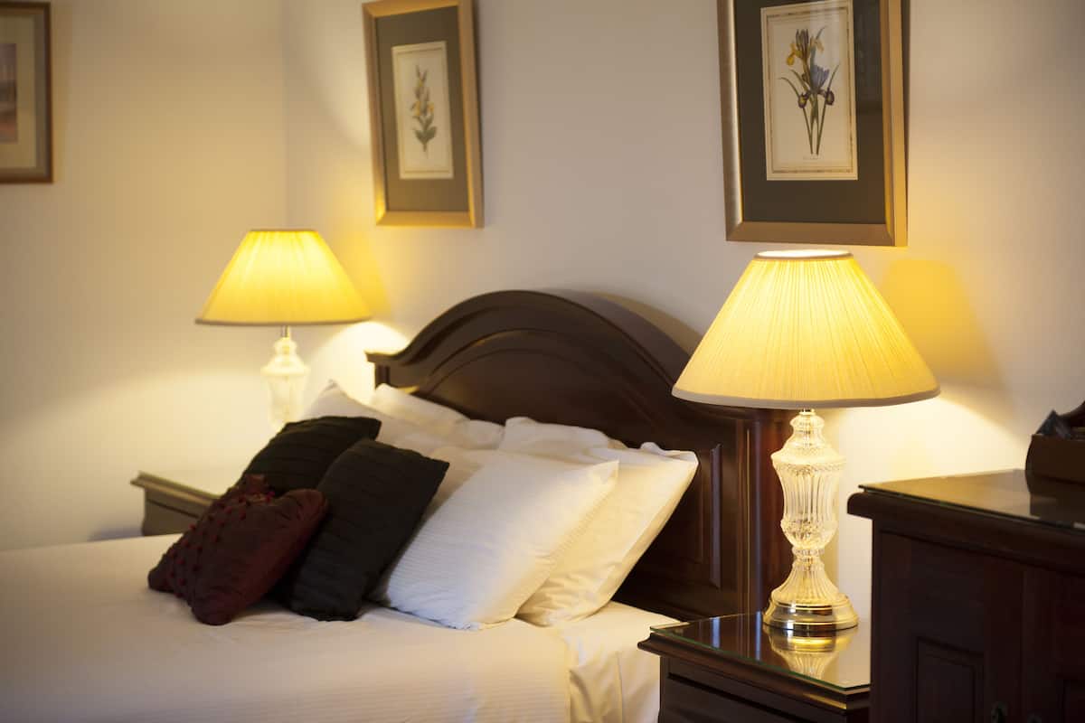 A neatly made bed with white and dark pillows, two bedside lamps, and framed artwork on the walls.