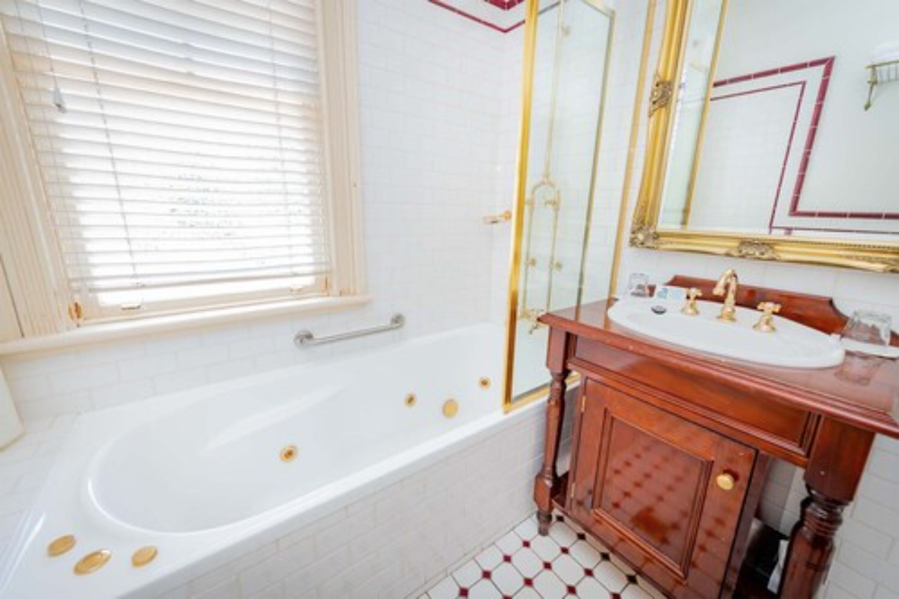 Un baño con bañera blanca, tocador de madera y un espejo grande con marco dorado.