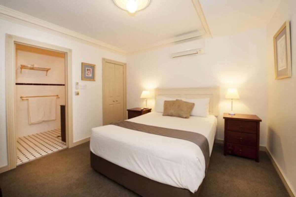 A bedroom with a large bed, two bedside tables with lamps, a door with a towel rack, and a wall-mounted air conditioner.