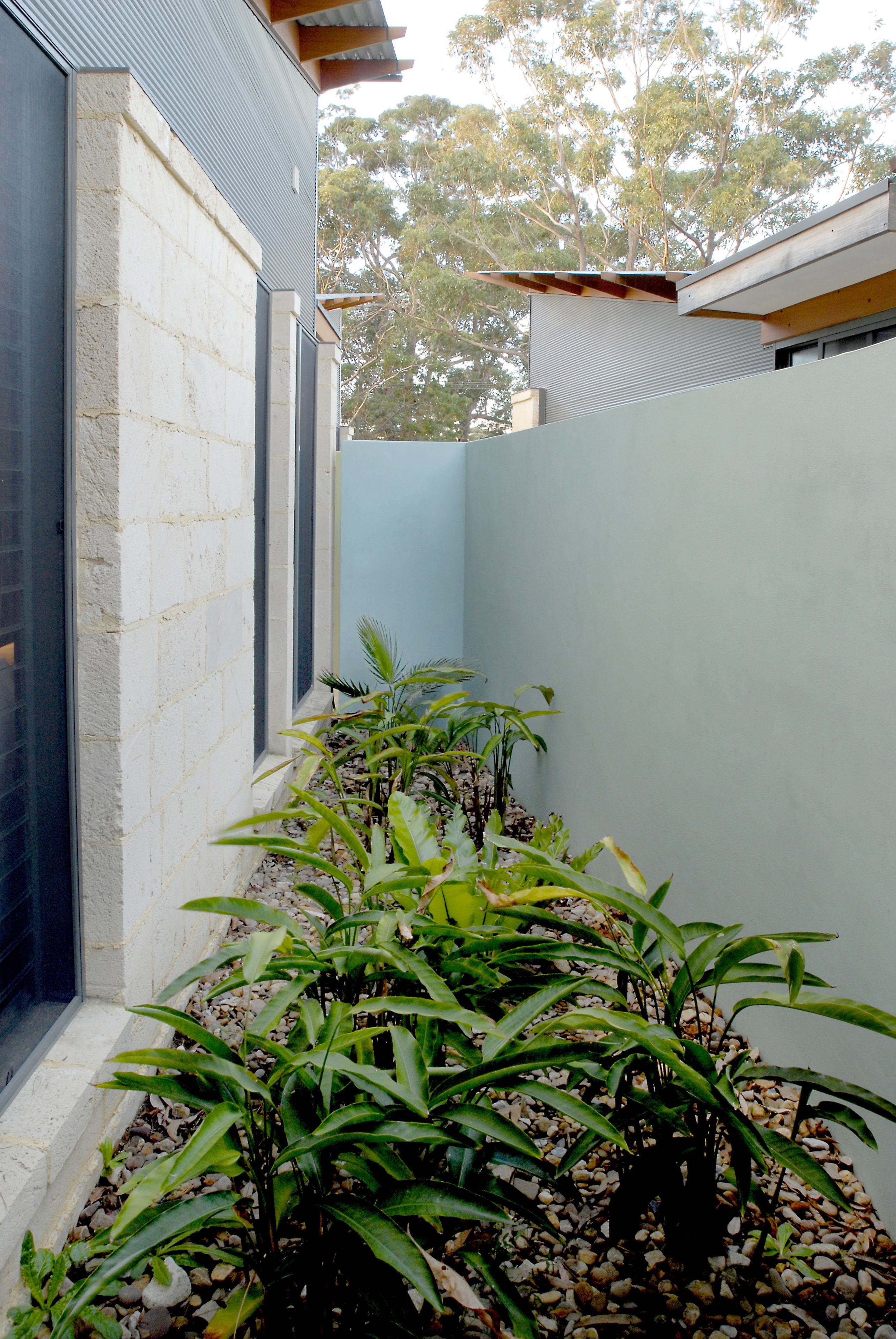 Un bâtiment moderne avec une façade en briques, un toit en métal et un espace jardin agrémenté de plantes vertes et de galets.