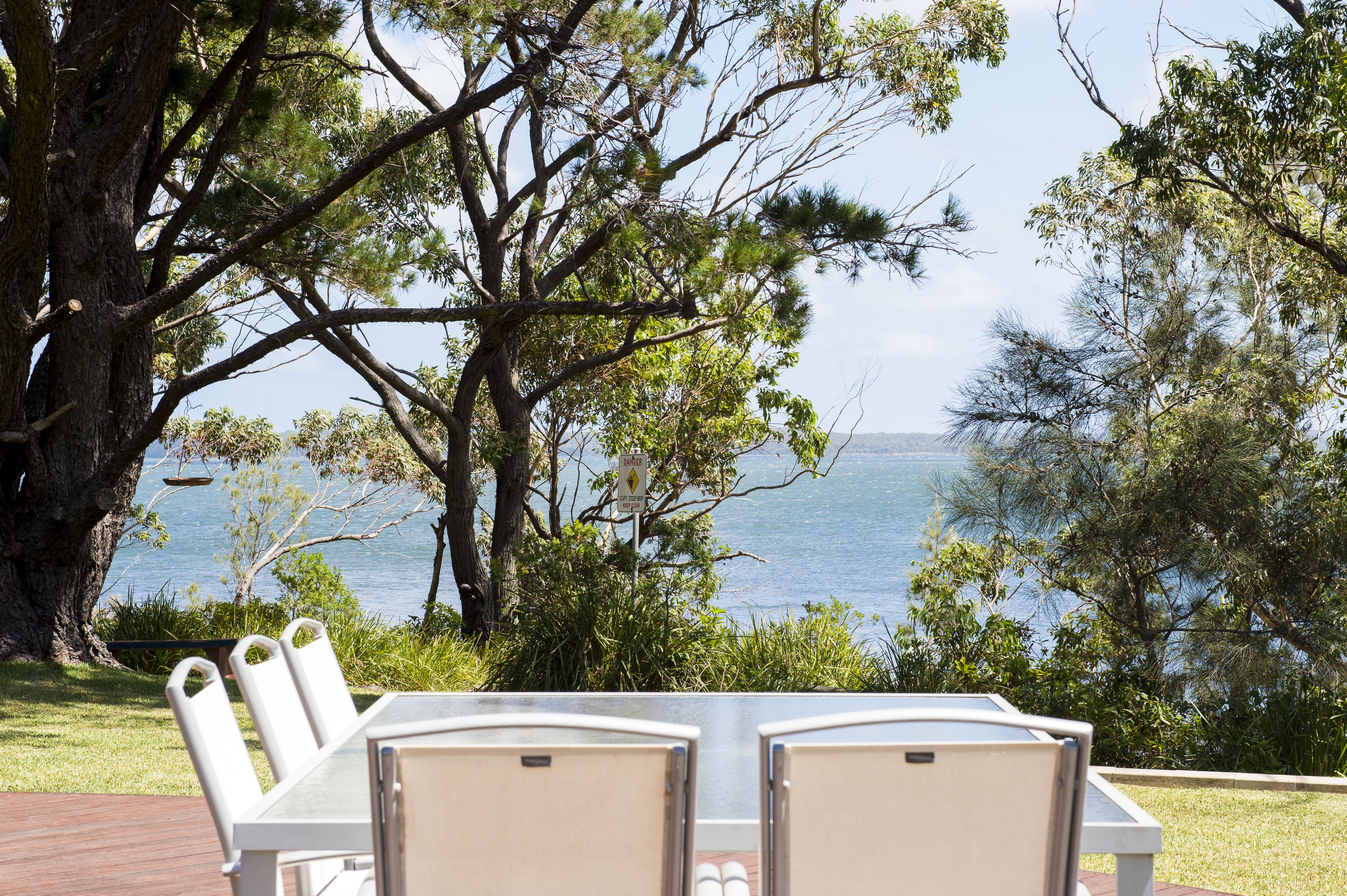A table with chairs set outdoors, overlooking a body of water with trees in the background.