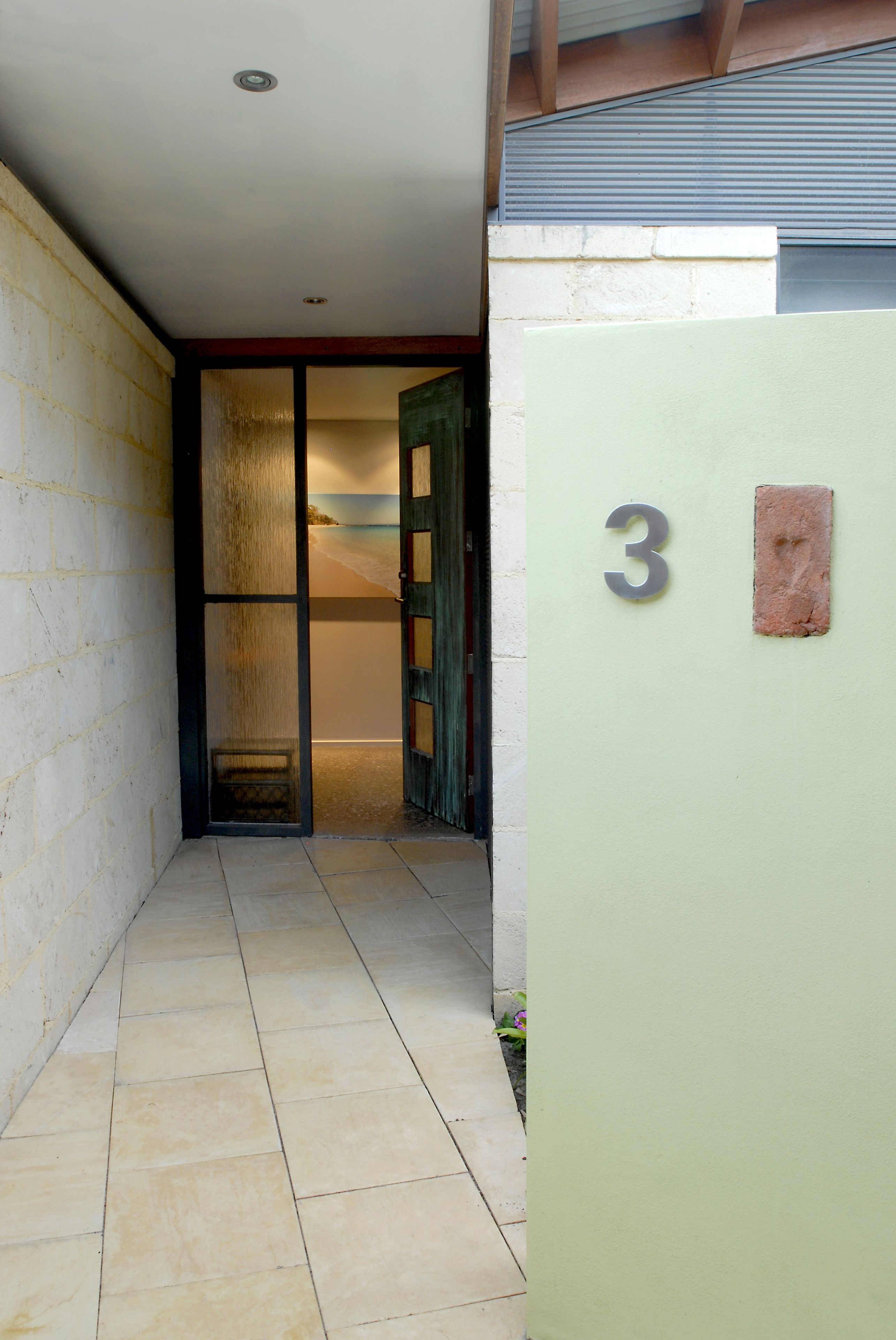 Un pasillo estrecho con suelo de baldosas que conduce a una habitación con puerta corredera. Se ve el número 3 en una pared.