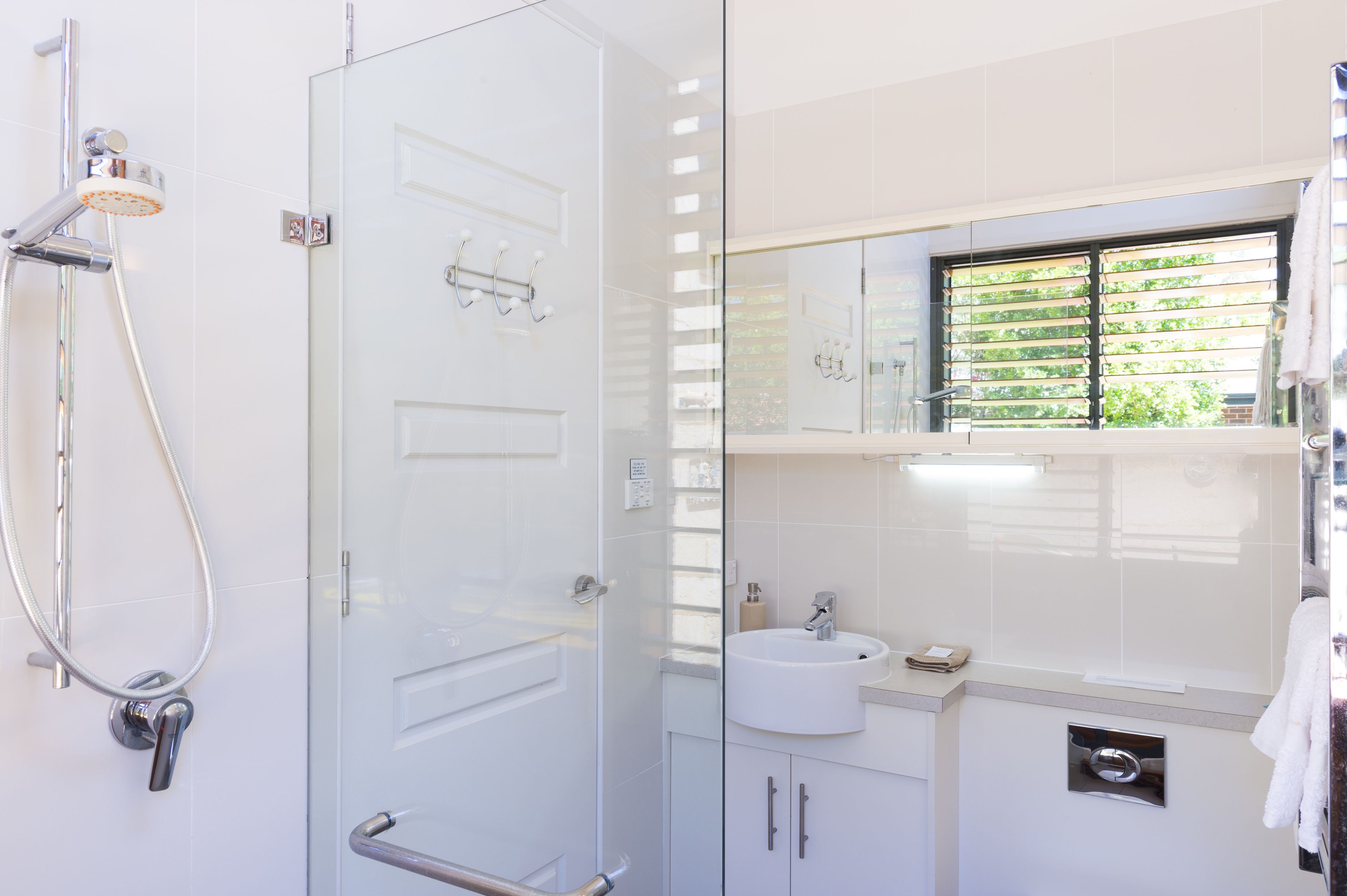 A modern bathroom with a glass shower enclosure, a white sink, and a window with blinds.