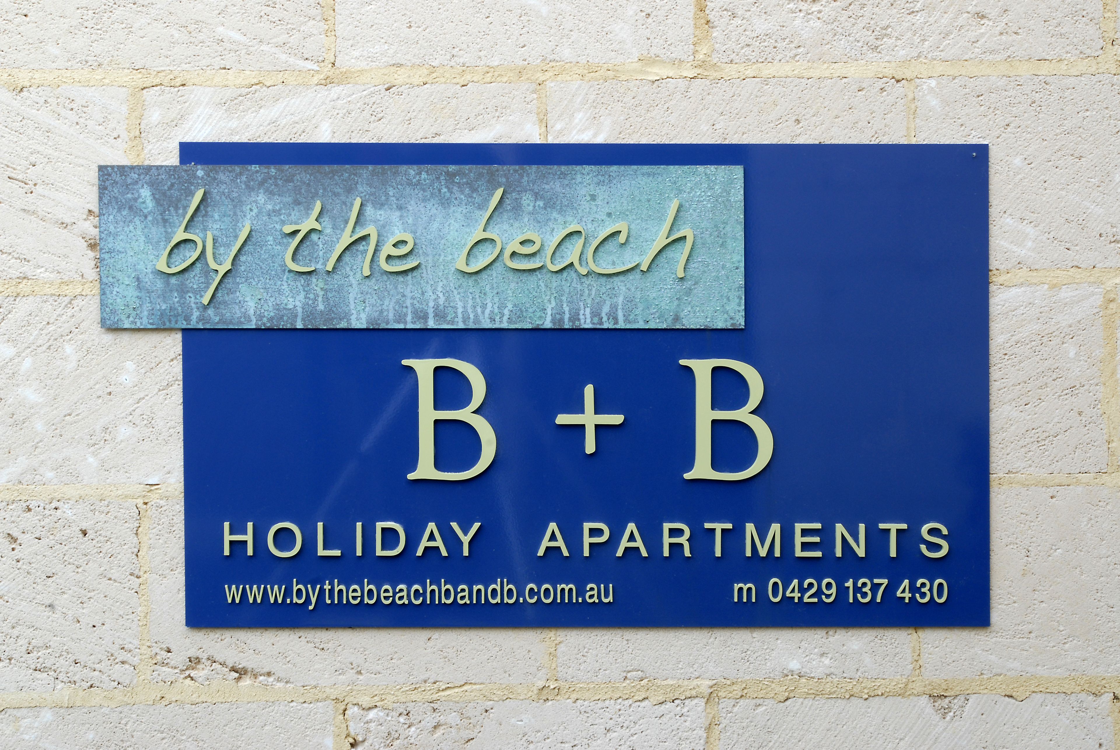 A sign for 'by the beach' holiday apartments with contact information.