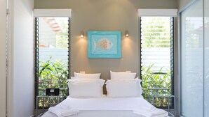 Een hotelkamer met een bed, twee nachtkastjes, een schilderij en uitzicht op groen door grote ramen.