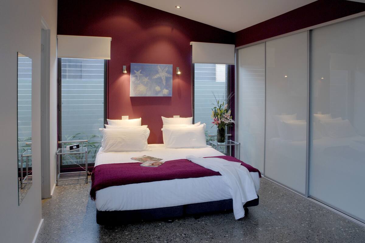 A modern bedroom with a large bed, a glass partition wall, and a view of the outside.