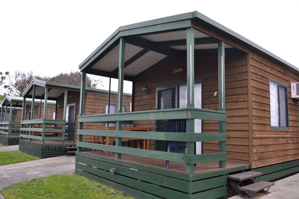 A row of wooden cabins with green railings and a covered porch.
