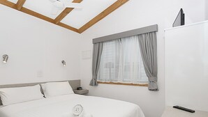 Ein Hotelzimmer mit Bett, Nachttisch, Fernseher und einem Fenster mit Vorhängen.