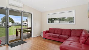 Ein geräumiges Wohnzimmer mit einem roten Ledersofa, einer Schiebetür zu einem Außenbereich und einem großen Fenster mit Blick hinaus.