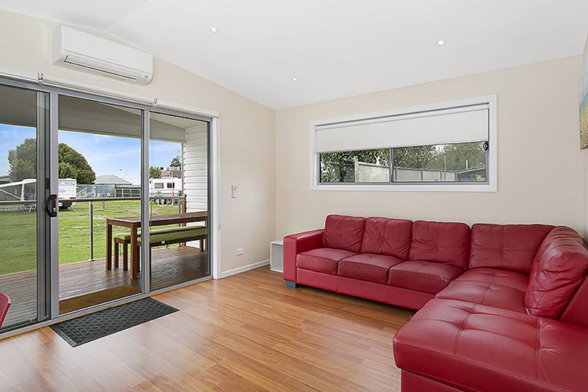 A spacious living room with a red leather sofa, a sliding glass door leading to an outdoor area, and a large window providing a view of the outside.