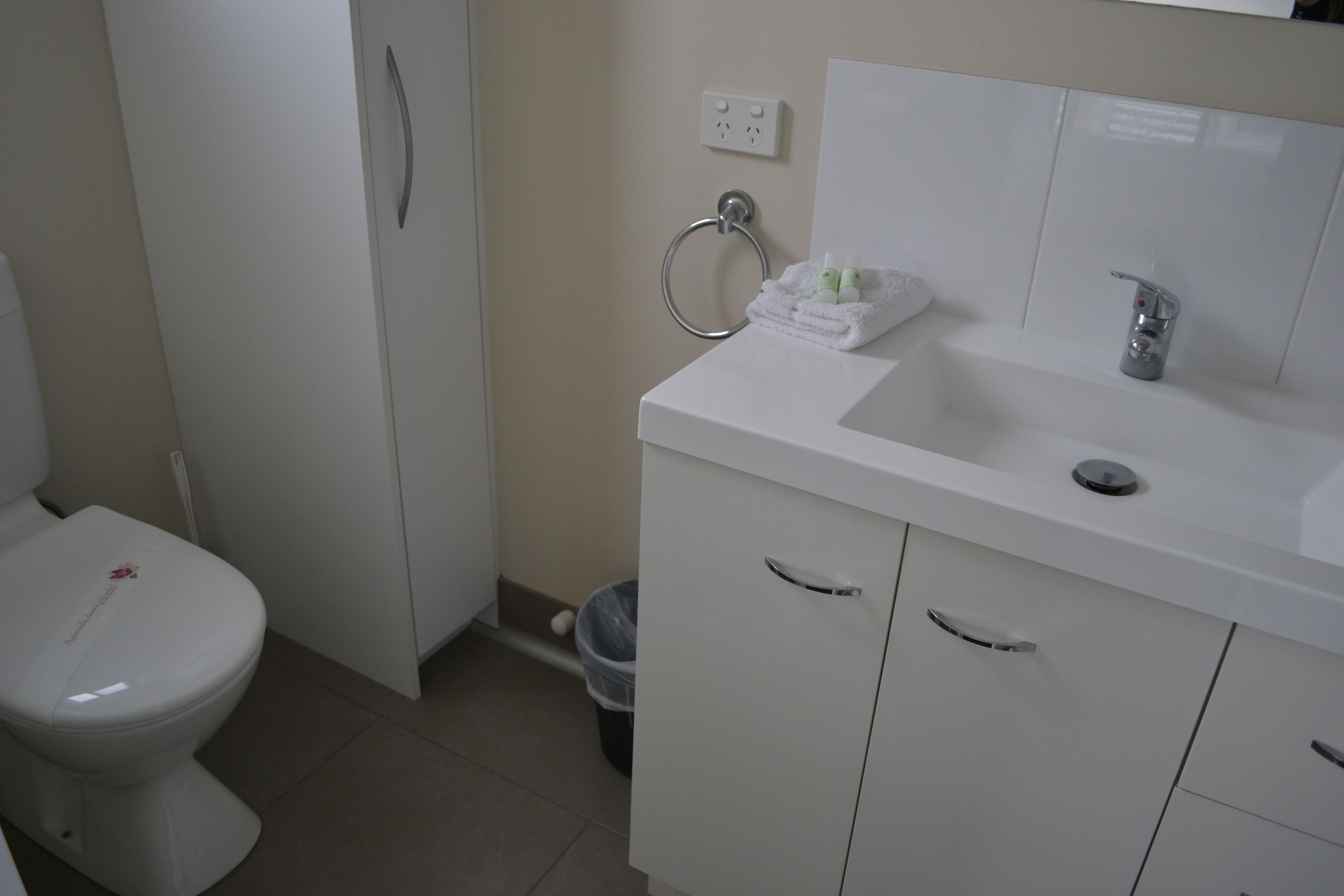 A bathroom with a white toilet, a sink with a mirror, and a trash can.