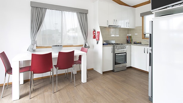 Eine moderne Küche mit weißen Schränken, einem Edelstahlherd und einem eingebauten Backofen. Es gibt einen Essbereich mit einem weißen Tisch und roten Stühlen.