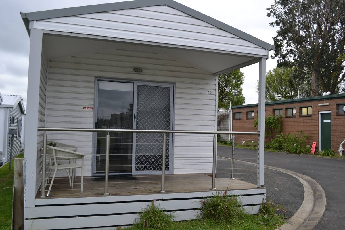 A small, single-story mobile home with a covered porch, a sliding glass door, and a small outdoor seating area.