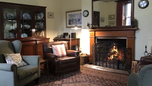 A cozy living room with a fireplace, leather armchairs, a patterned rug, and a china cabinet. - Victoria House (Portland)