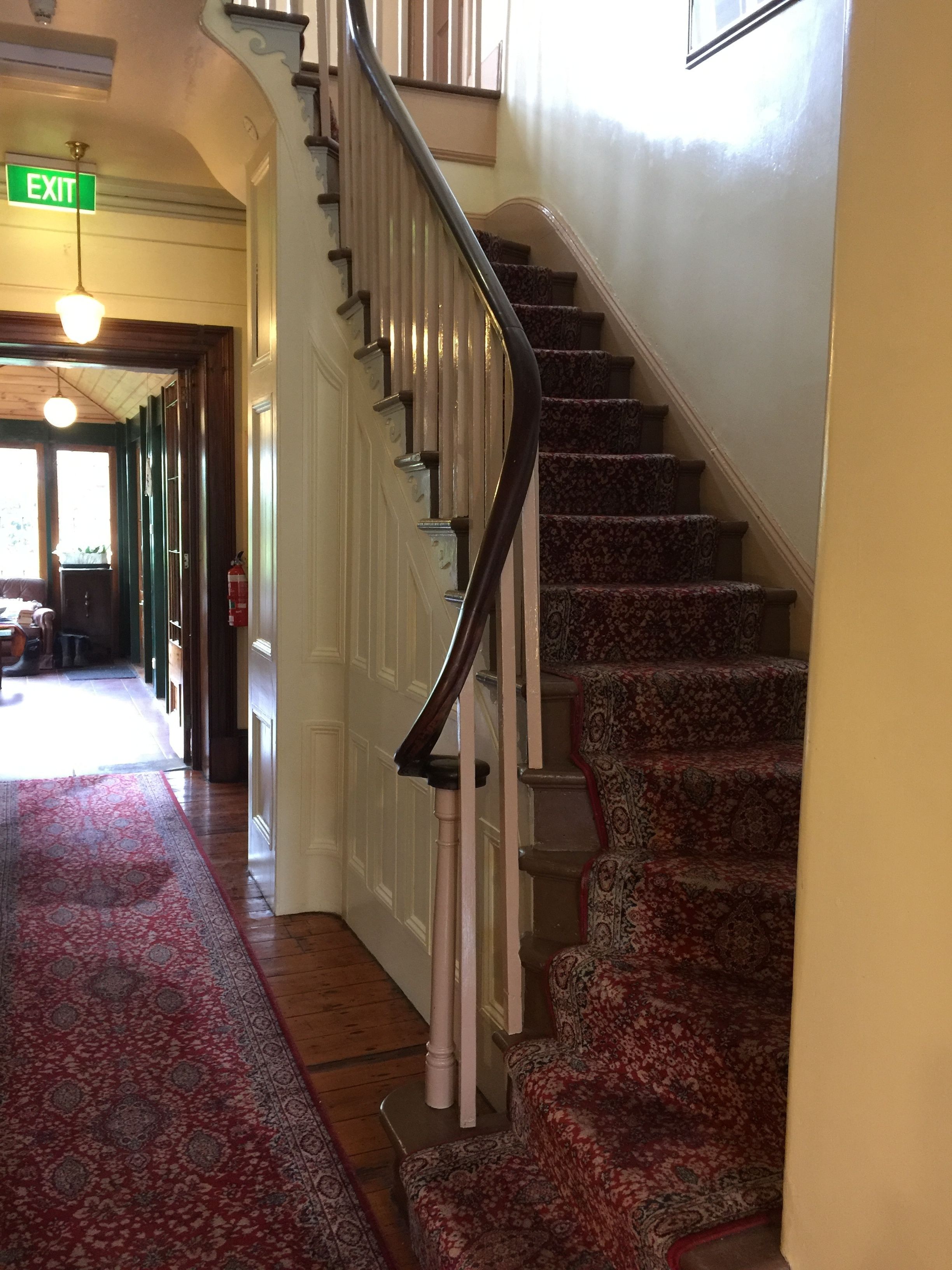 A staircase with a handrail, carpeted steps, and a door with an exit sign.