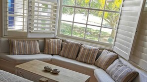 A cozy seating area with a wooden coffee table, a cushioned bench, and a window with blinds. - Arcadia House (Byron Bay)