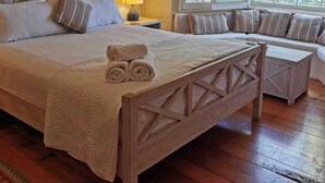 A bedroom with a wooden bed, a bench, a window with blinds, and a wall-mounted air conditioner. - Arcadia House (Byron Bay)