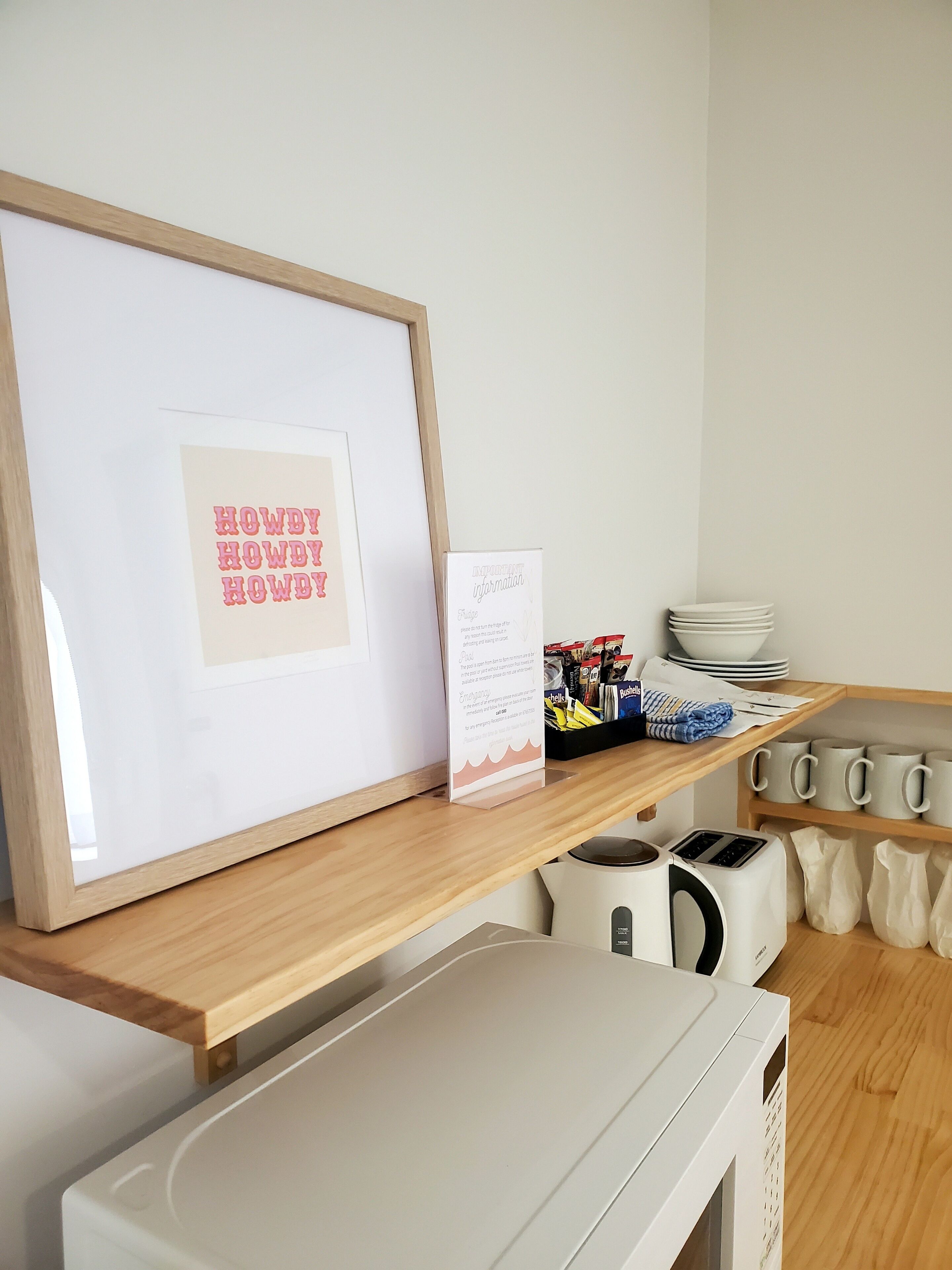 Eine Küchenzeile mit einem gerahmten Bild, einem Schild, einem Toaster, einem Wasserkocher und einem Stapel Teller auf einem Holzregal.