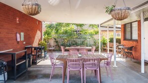 Un espace extérieur aménag é en patio, avec un mur en briques, des tables, des chaises, des suspensions florales et des plantes en pot.