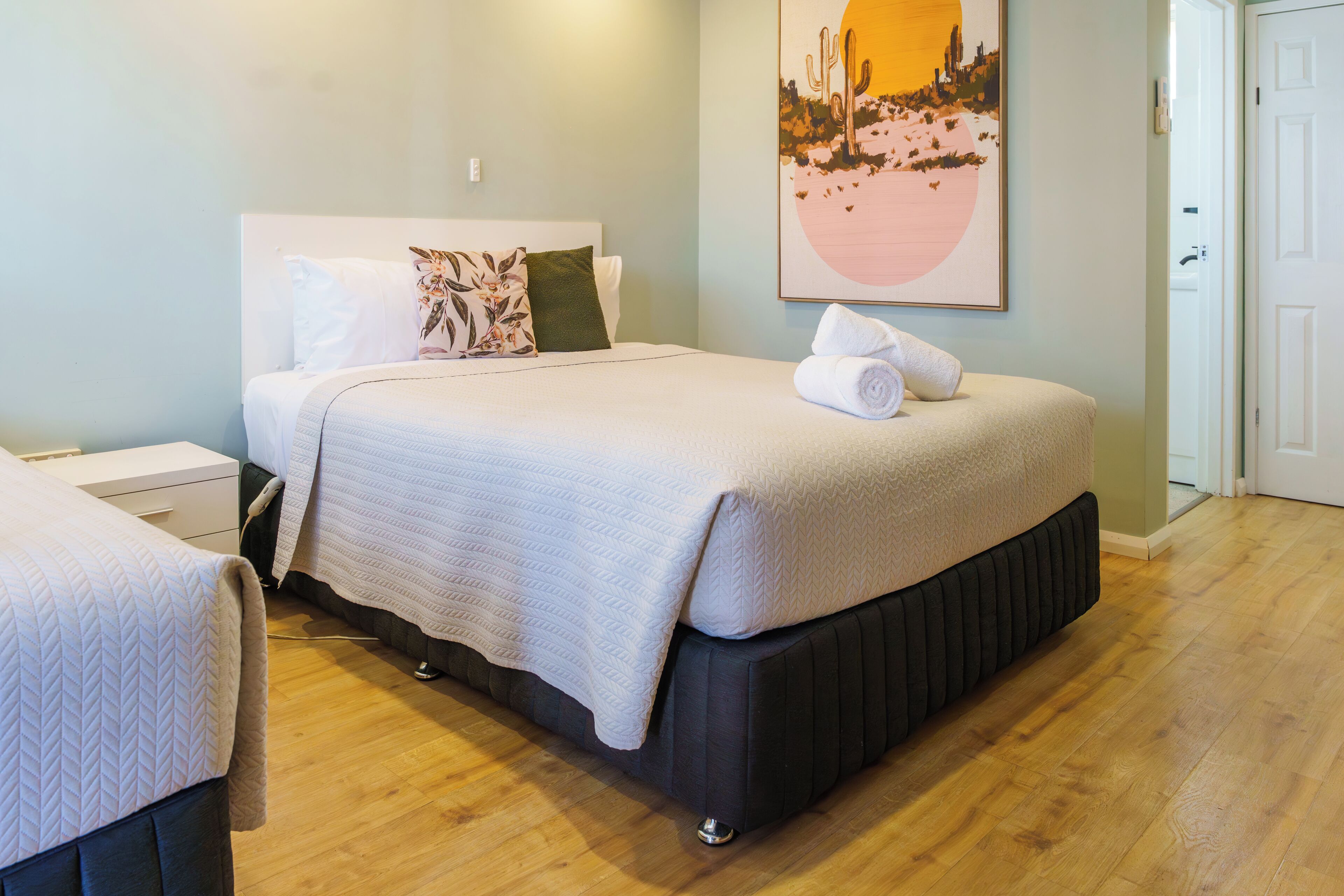 A neatly made bed with a white quilt, a pillow, and a rolled towel on the side.