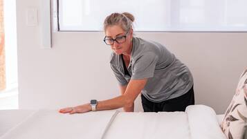 A person adjusting a bed in a room with a window and a plain wall.