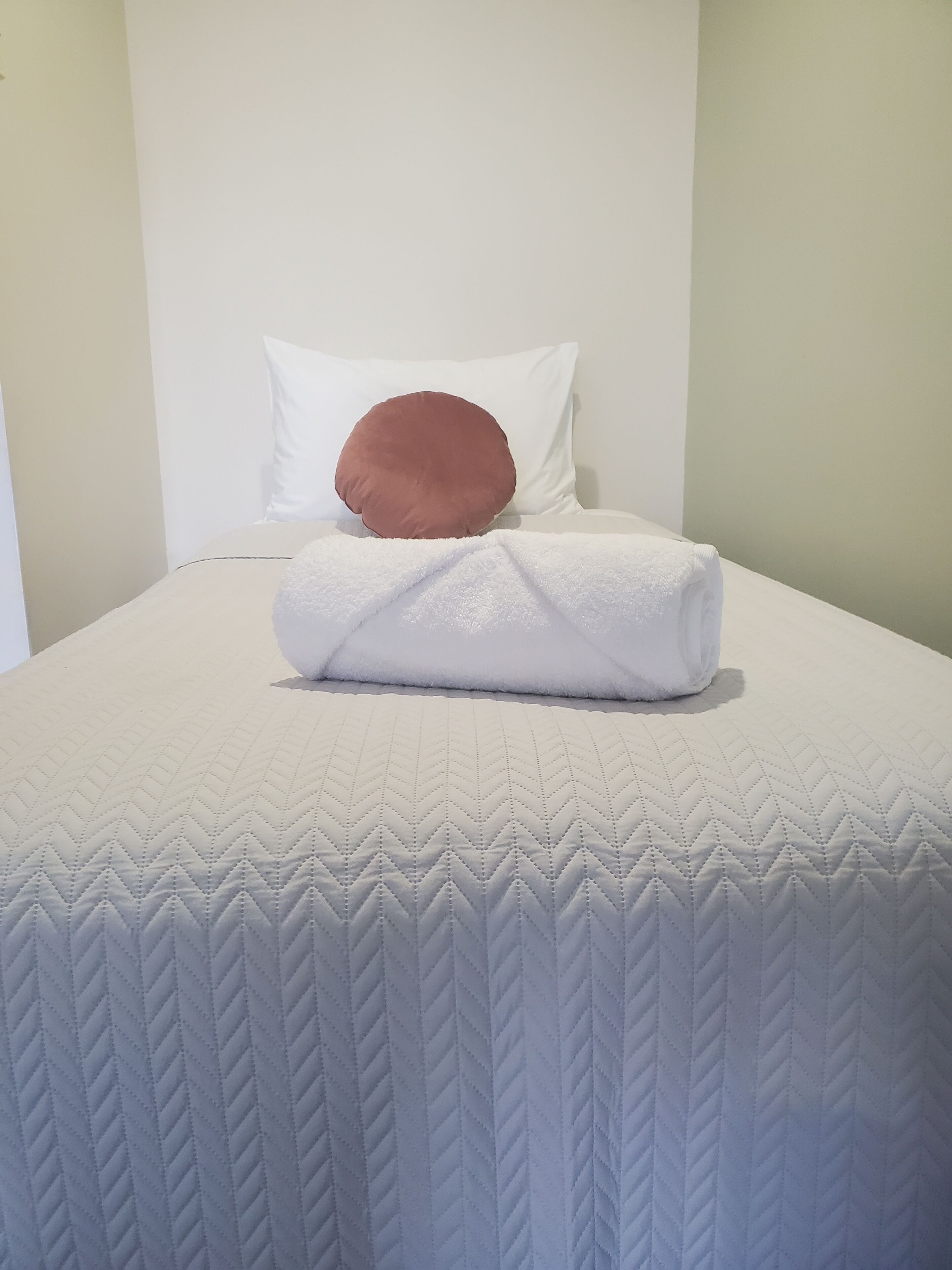 A neatly made bed with a white quilt and a brown pillow.