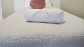 A neatly made bed with a white quilt and a brown pillow.