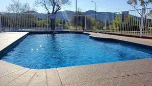 Une piscine rectangulaire avec une terrasse carrelée, entourée d’une clôture métallique, et un panneau d’avertissement bien visible.