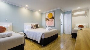 Une chambre d’hôtel avec deux lits, un plancher en bois, un grand tableau et un appareil de climatisation.