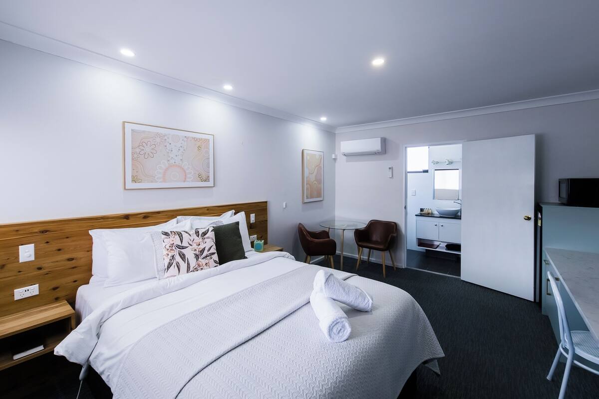 A hotel room with a bed, a desk, a chair, and a bathroom visible through an open door.
