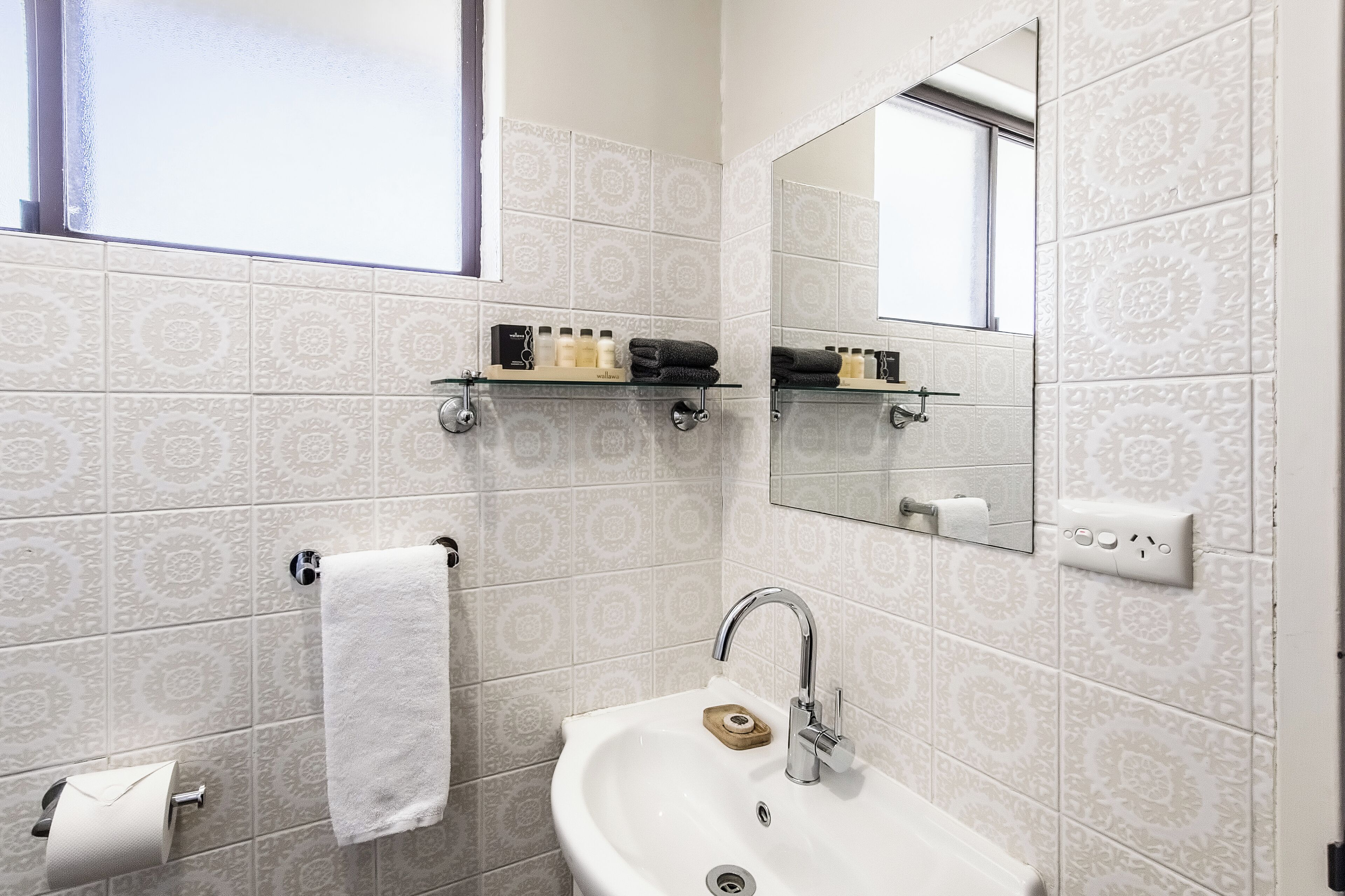 Een badkamer met betegelde vloer, een wastafel, een spiegel en planken met toiletartikelen.