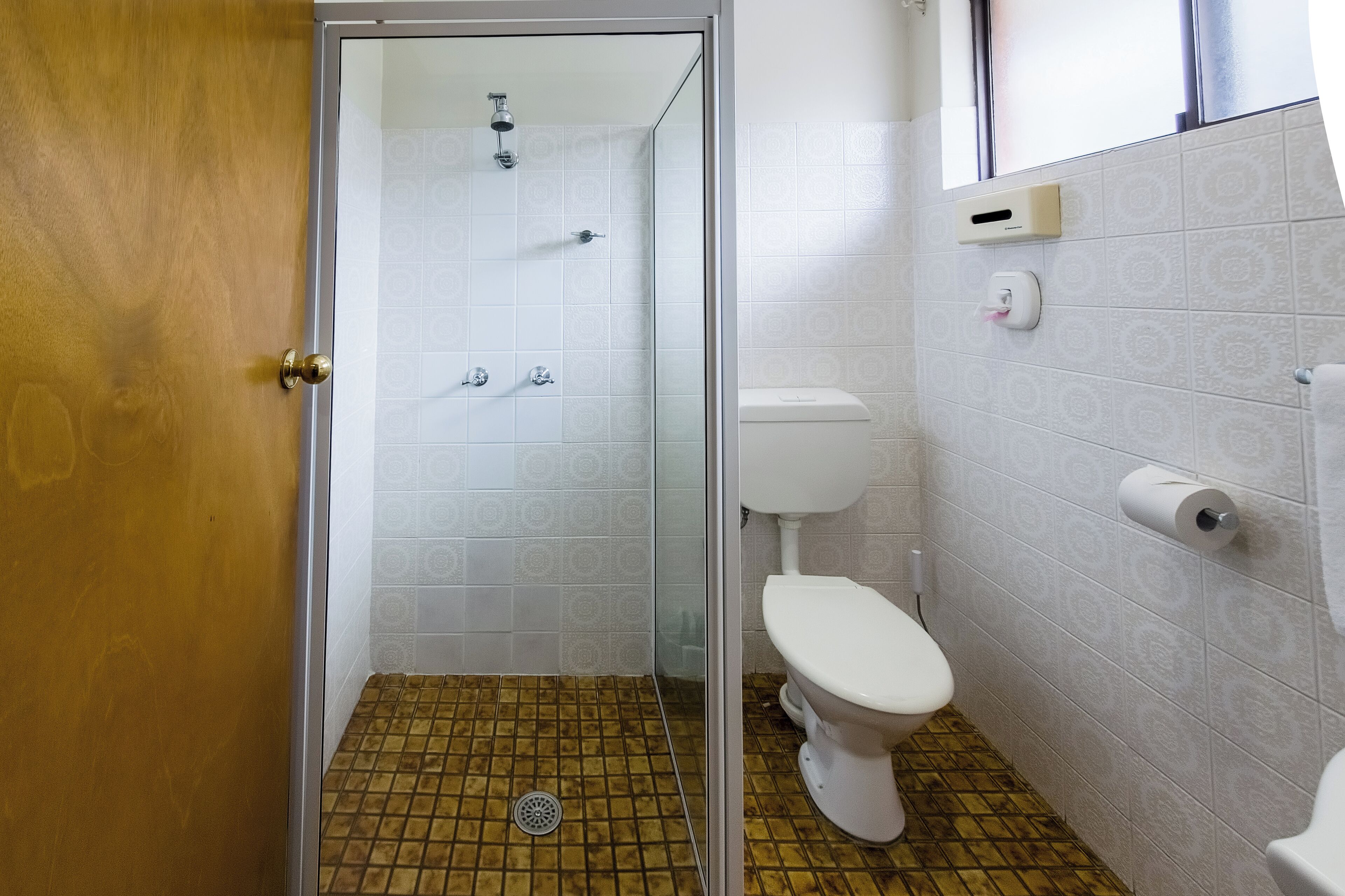 Et badeværelse med brusebad, toilet og gulvfliser med mønster.
