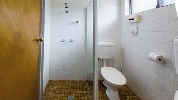 Et badeværelse med brusebad, toilet og gulvfliser med mønster.