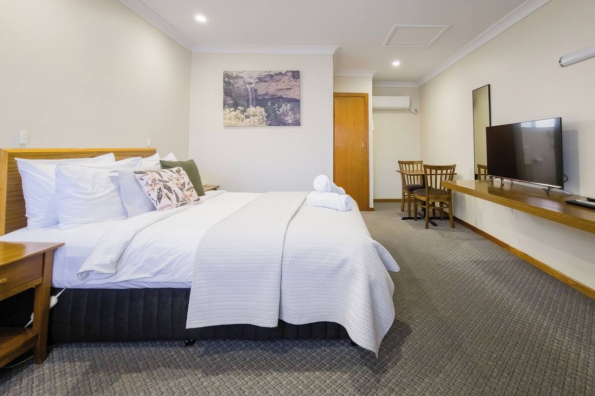 A hotel room with a bed, a TV, a desk, and a chair.