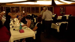 Un restaurante con varias mesas dispuestas para comer, un camarero atendiendo a los comensales y un hombre de pie cerca de la entrada.