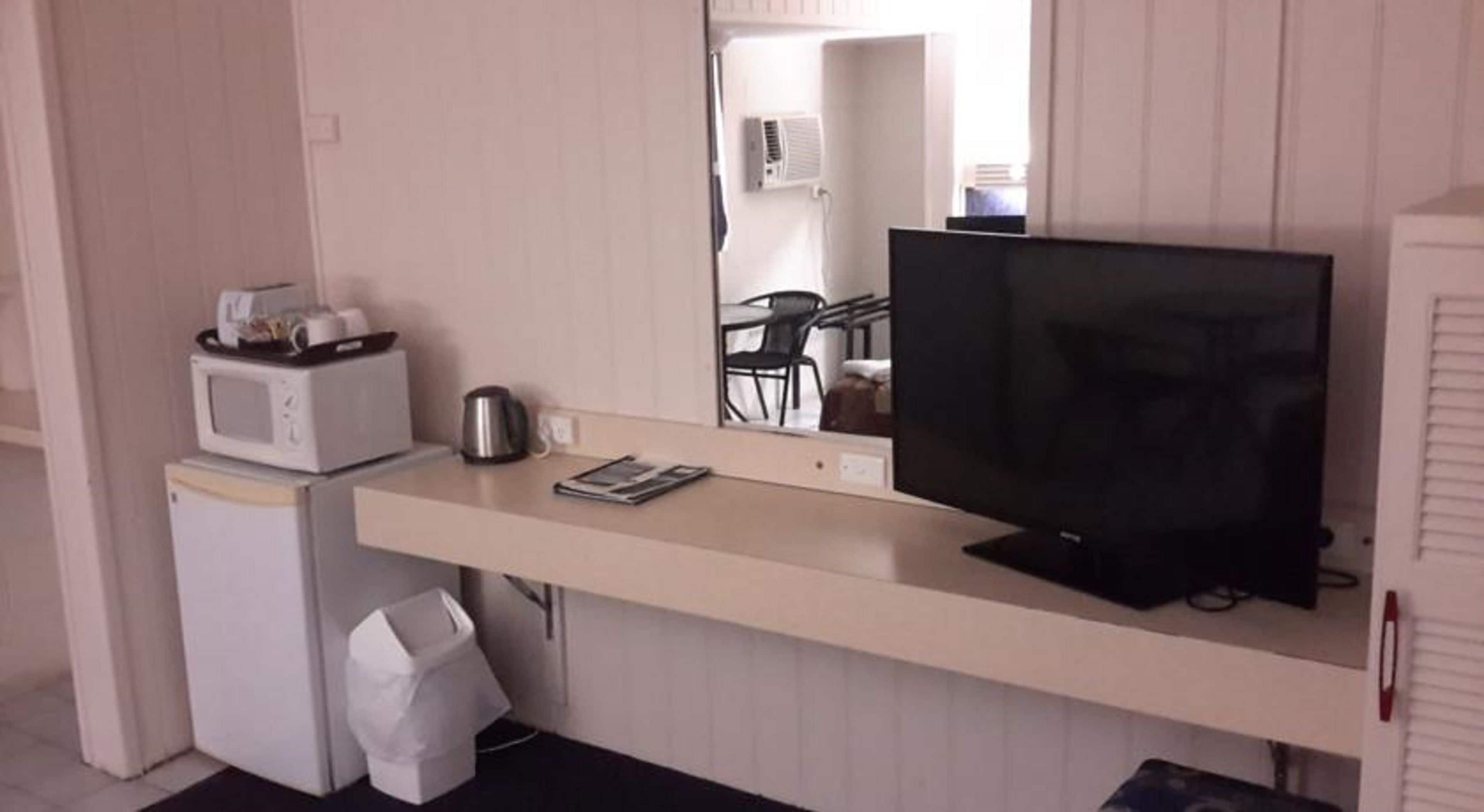 A compact kitchenette with a microwave, kettle, and small refrigerator. A flat-screen TV is mounted on the wall above a counter.
