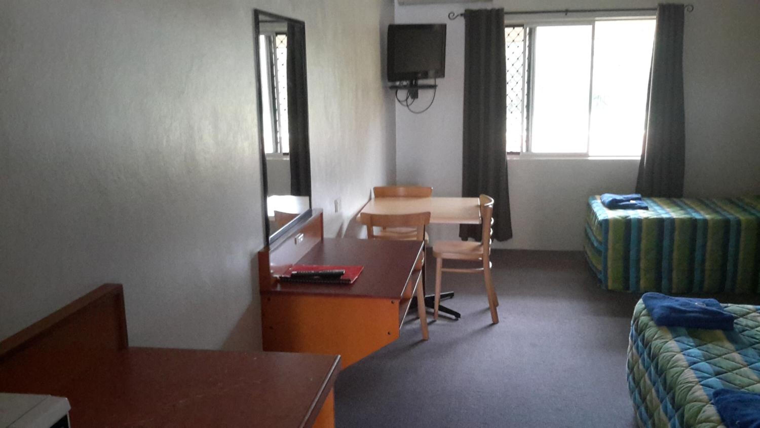 A hotel room with a desk, chair, bed, TV, and a window with curtains.