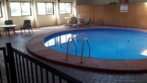 Una piscina interior con borde de azulejos, una escalera de piscina y sillas de descanso.