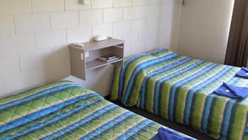 A dormitory room with two beds, each with a striped green and blue comforter. There is a shelf with a book and a phone on it.