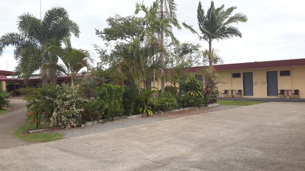 Un edificio con varias habitaciones, un camino de entrada pavimentado y diversas plantas tropicales.