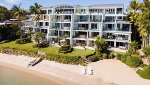 Un hôtel à plusieurs étages, doté de balcons, offrant une vue sur la plage et comprenant un jardin bien entretenu.