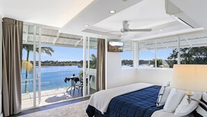 Une chambre dotée d’un grand lit, d’un ventilateur de plafond et offrant une vue sur une piscine et une plage.