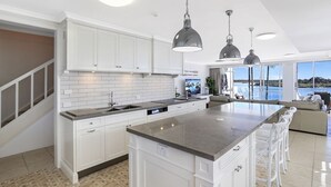 Une cuisine moderne avec des meubles blancs, un grand îlot central et des luminaires suspendus.