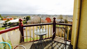 A balcony with a table and chairs, overlooking a town with houses and a church. - The Manse (Daylesford)