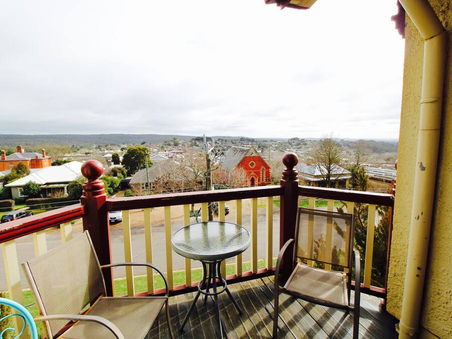 A balcony with a table and chairs, overlooking a town with houses and a church.