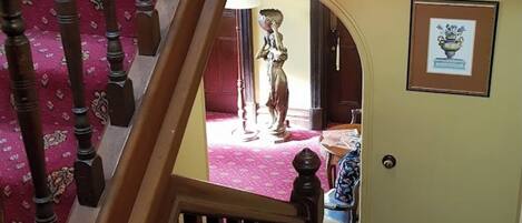 A wooden staircase with a red carpet leading to a room with a door and a framed picture on the wall.