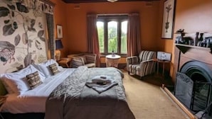 A hotel room with a bed, a sofa, a chair, a small table, a fireplace, and a window with curtains. - The Manse (Daylesford)