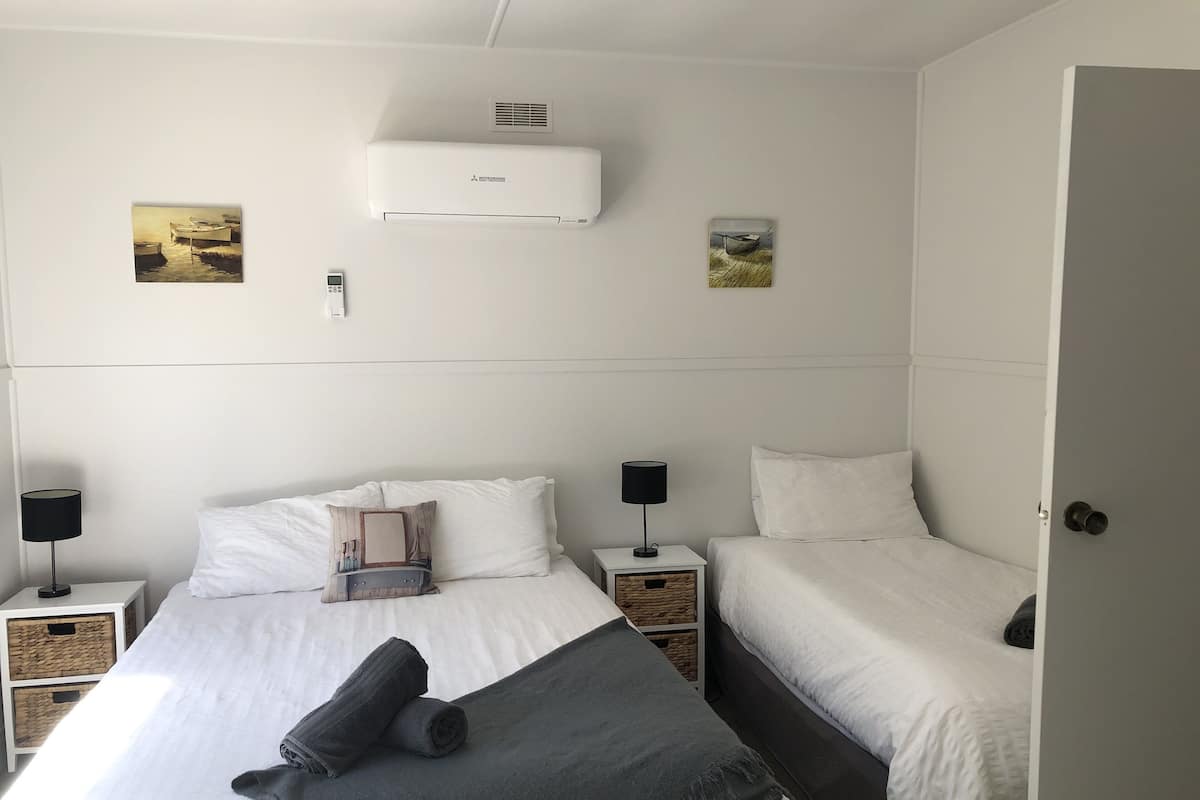 Une chambre d’hôtel comprenant un lit, deux tables de chevet, une lampe, un radiateur et deux climatiseurs fixés au mur.